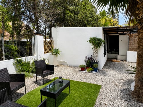Modern apartment patio with black seating, artificial grass, white structure, potted plants, and palm trees at Apartamentos