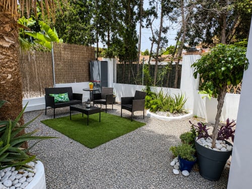 Modern patio garden with black furniture, artificial turf, potted plants, and white fencing at Apartamentos Turísticos