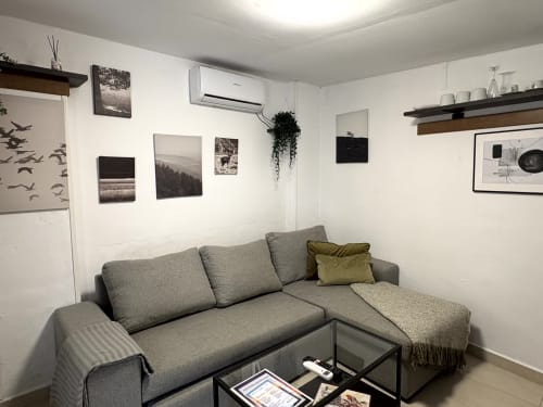 Modern living room with gray L-shaped sofa, wall art, and air conditioning in Almayate Alto apartment