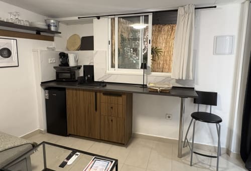 Modern kitchenette with wooden cabinets and black countertop in Almayate Alto beach apartment, featuring stool seating and