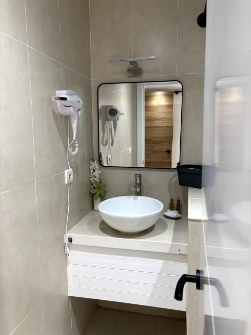 Modern bathroom with white round sink, black-framed mirror, beige tiled walls and white vanity in Almayate Alto apartment