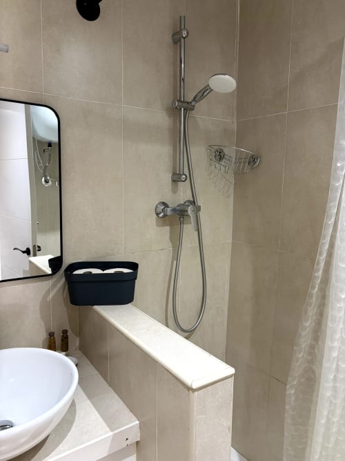 Modern bathroom shower with chrome fixtures, black storage basket, and beige tile walls in Apartamentos Turísticos Axarent