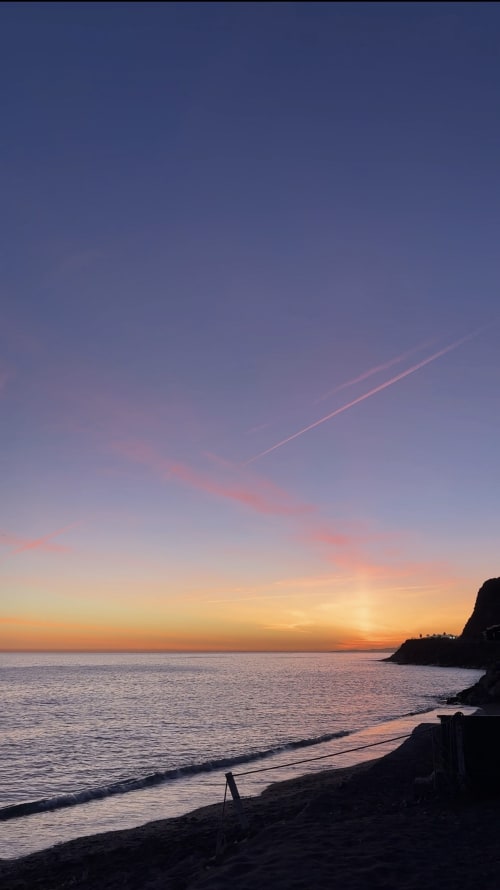 Sunset over the Mediterranean Sea at Almayate beach with golden and pink sky, silhouetted coastal cliffs and calm waters