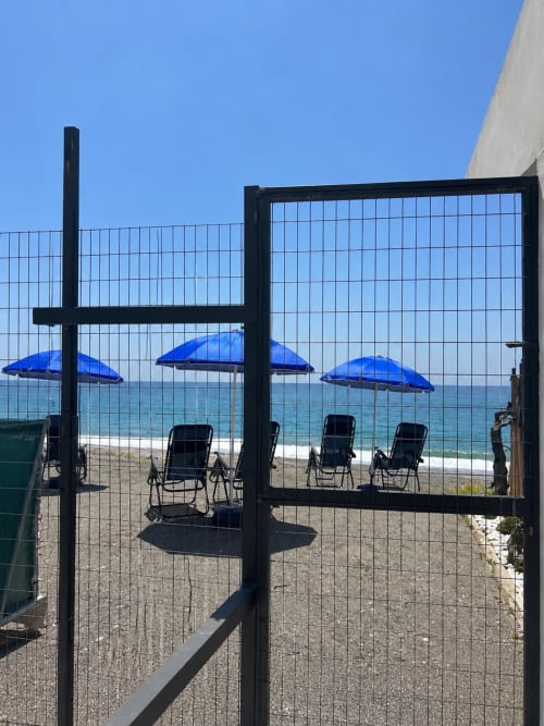 Puerta de acceso a la playa de Apartamentos Turísticos Axarent con sombrillas azules y tumbonas con vistas a la playa de Almayate