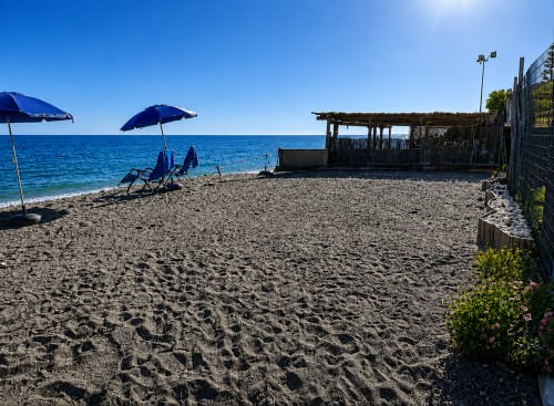 Sandy beach at Almayate Alto with blue umbrellas, lounge chairs, wooden beach shack, and calm Mediterranean Sea under clear