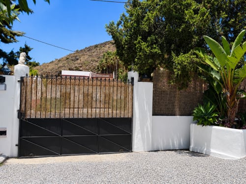 Modern white-walled apartment entrance with black gate and wooden trellis at Apartamentos Turísticos Axarent, Almayate Alto,