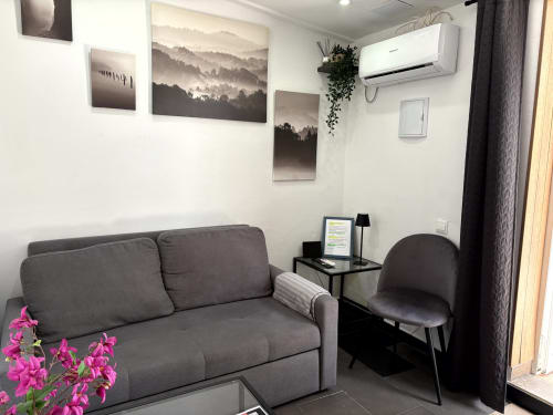 Modern living room with gray sofa, armchair, mountain landscape artwork, and air conditioning at Apartamentos Turísticos