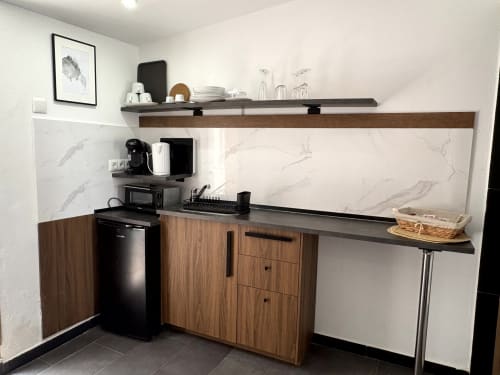 Modern kitchenette with wooden cabinets, marble backsplash, black appliances and open shelving at Apartamentos Turísticos