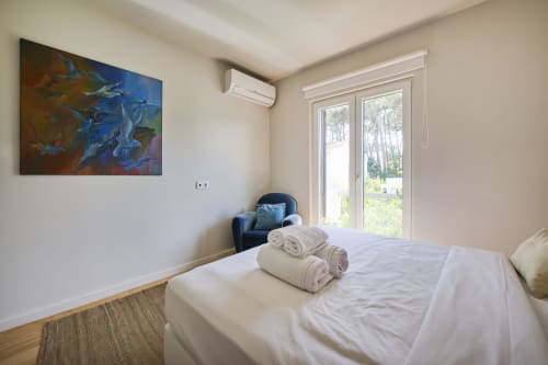 Habitación moderna en Republica do Sul con ropa de cama blanca, toallas enrolladas, obra azul, aire acondicionado y puertas de cristal hacia la piscina