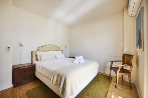 Dormitorio luminoso en villa d'Aura Aroeira con cama tapizada en crema, mesita de noche de madera y butaca en resort Republica do Sul