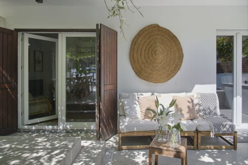 Patio de villa moderna en Republica do Sul con tumbona de madera, cojines blancos, arte tejido redondo en pared y puertas de vidrio que se abren