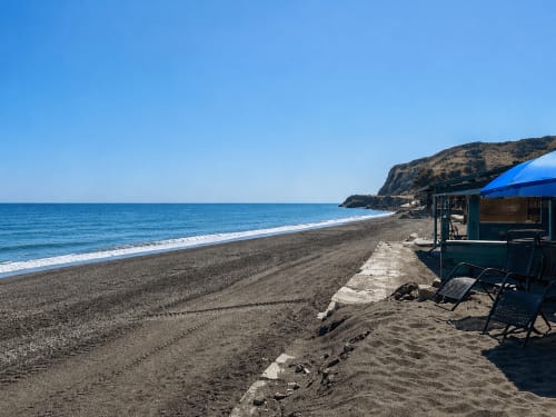 Almayate beach with dark sand, blue sea, rocky cliff, beachfront apartment complex with blue umbrellas