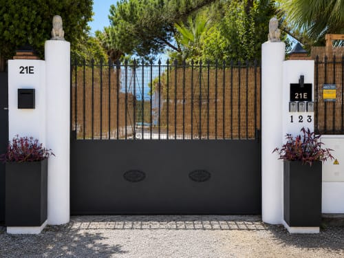 Modern gated entrance to Apartamentos Turísticos Axarent with white pillars, black metal gate, and Mediterranean sea view