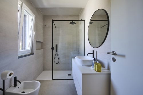Baño moderno en villa Republica do Sul, Aroeira, con tocador blanco, espejo redondo, ducha tipo walk-in y luz natural