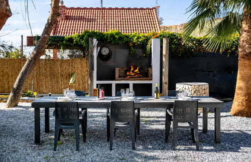 Outdoor dining patio at Apartamentos Axarent with fireplace, black table, chairs, and ivy-covered structure in Almayate Alto.