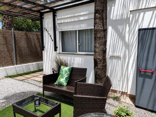 Patio seating area at Apartamentos Axarent with black wicker furniture, palm tree, and white-walled apartment in Almayate