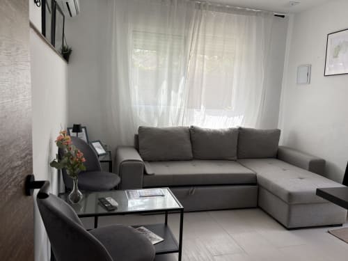 Modern living room with gray sectional sofa, black coffee table, and sheer curtains overlooking sea view at Apartamentos