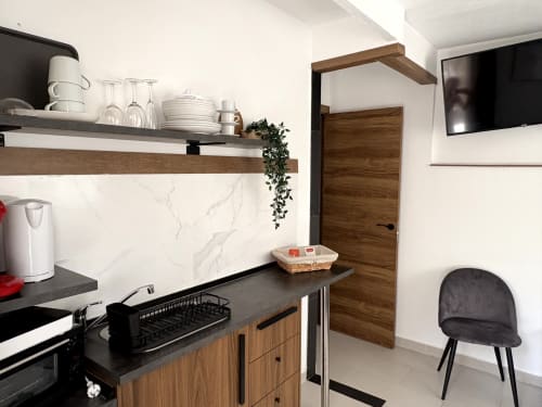 Modern kitchenette in Almayate Alto apartment with black countertop, wooden cabinetry, marble backsplash, and TV mounted on