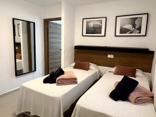 Twin bedroom with white bedding, wooden headboard, and black and white framed photos in Almayate Alto apartment