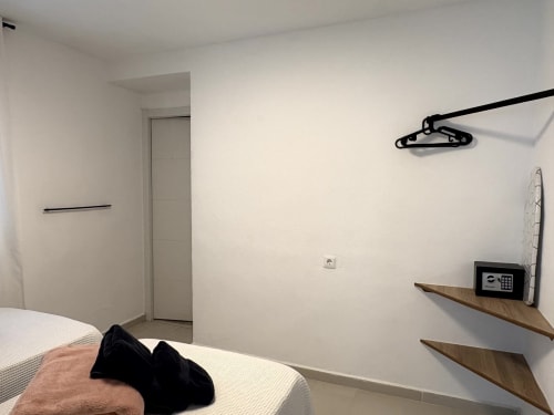 Modern bedroom in Almayate Alto apartment with bed, wall-mounted shower rack, wooden shelves, and safe.