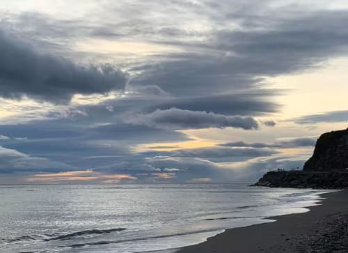 Dramatic sunset over Almayate beach with stormy clouds, rocky cliffs, and calm waves at Apartamentos Turísticos Axarent