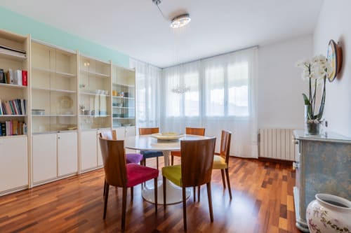 Esszimmer Casa Pleiadi im Prince Garda Sirmione mit rundem Tisch, farbigen Stühlen, Holzregalen und Gartenblick