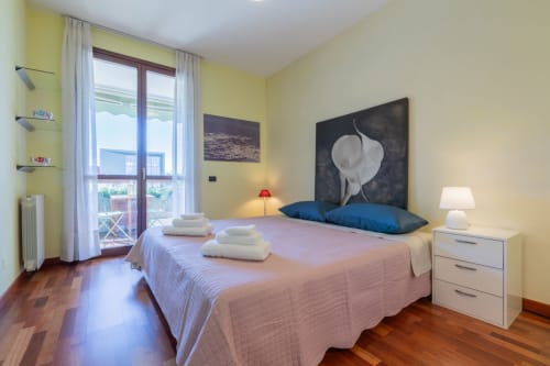 Helles Schlafzimmer im Prince Garda in Sirmione mit gelben Wänden, Doppelbett, blauen Kissen und Balkon mit Gartenblick