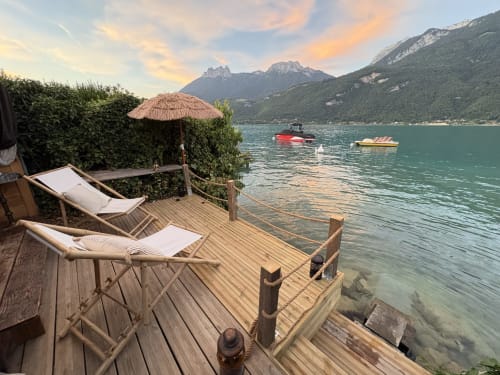 Terrasse en bois avec transats et parasol surplombant le lac turquoise et les montagnes au gîte de Chaparon, Lathuile
