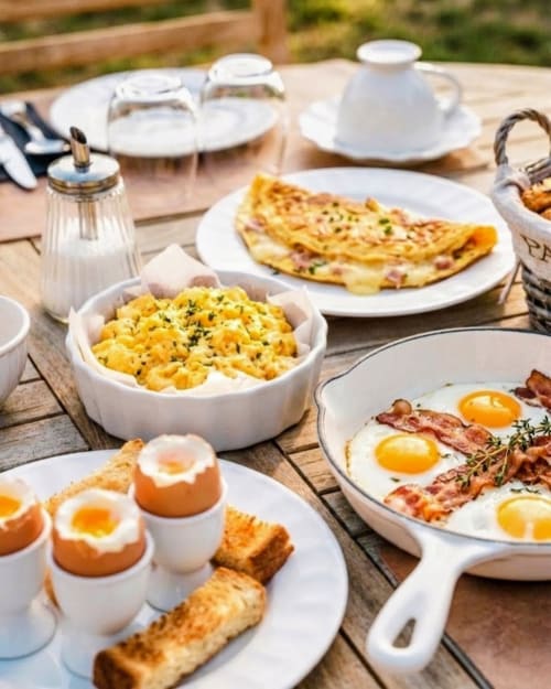 Gourmet breakfast spread at Loup Castel Boutique Hotel featuring eggs, bacon, omelette, and toast on wooden table