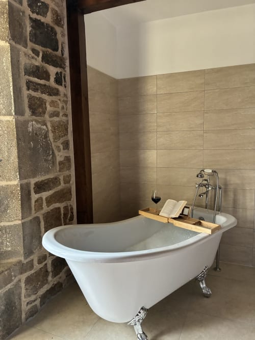 Baignoire de luxe à pieds griffus dans la Chambre Royale du Manoir de Fornebello, aux murs de pierre et plateau de bain en bois