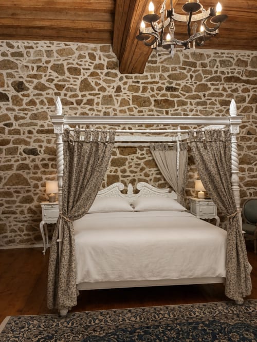 Lit à baldaquin élégant aux draps crème dans la Chambre Royale aux murs de pierre du Manoir de Fornebello, manoir de campagne français