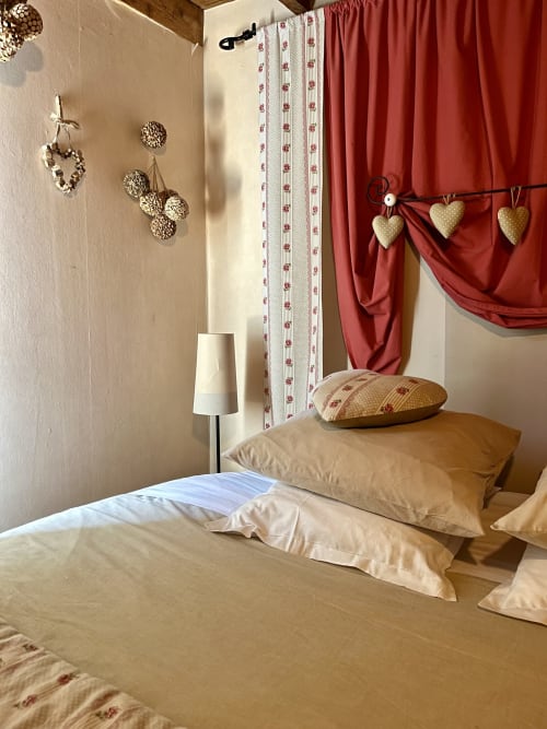 Chambre douillette au Domaine De La Ferme De Ribeaufontaine avec parure beige, rideaux rouges et décors en forme de cœur