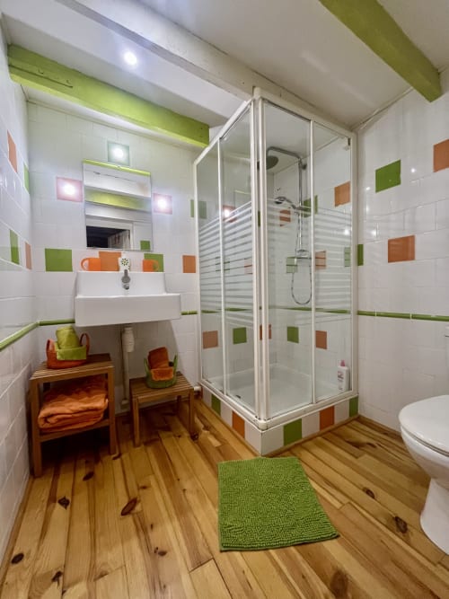 Salle de bain moderne avec carrelage vert et orange, douche à l'italienne et parquet à Domaine De La Ferme De Ribeaufontaine