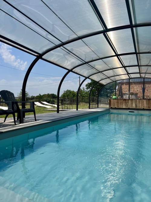 Piscine couverte du Domaine De La Ferme De Ribeaufontaine avec eau turquoise, transats et vue sur la campagne