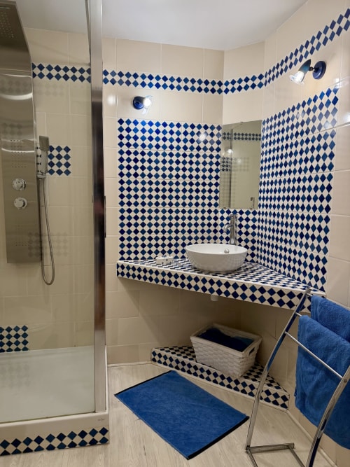 Salle de bain moderne avec carrelage géométrique bleu et blanc, vasque, douche à l'italienne et serviettes bleues à la Domaine De La Ferme