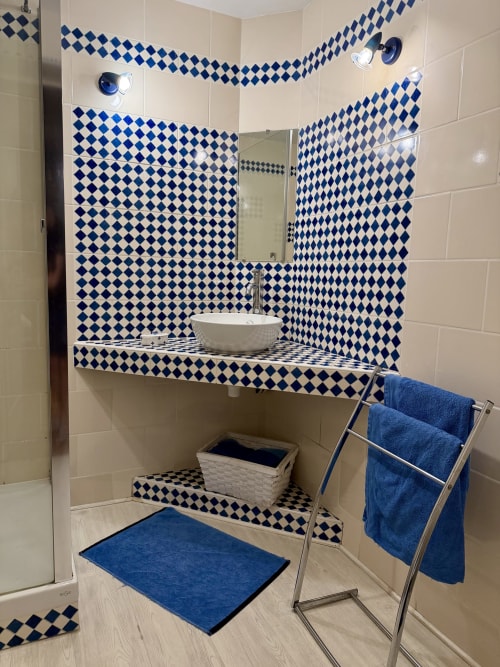 Salle de bain élégante avec carrelage losange bleu et blanc, vasque, miroir, porte-serviettes avec serviettes bleues et baignoire bleue