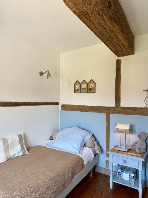 Chambre charmante de gîte français avec poutres apparentes, murs bleus en partie basse, lit simple aux oreillers bleus, style rustique