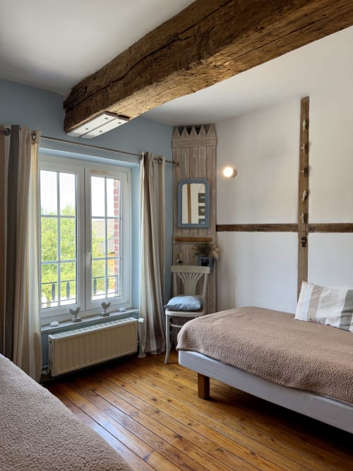 Chambre rustique avec plafond aux poutres apparentes, murs gris-bleu, parquet et fenêtres vue jardin au Domaine De La