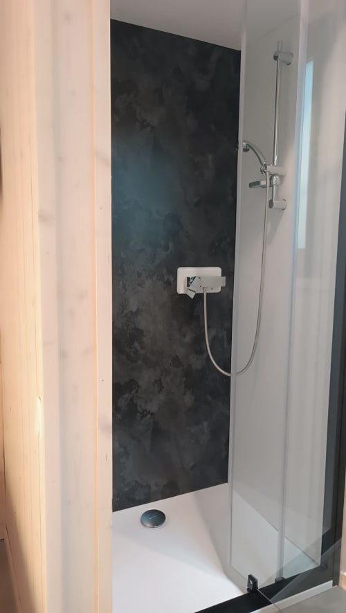 Douche moderne à la villa Les Chalets Du Lac avec mur d'accent en carrelage foncé, porte en verre et pomme de douche effet pluie