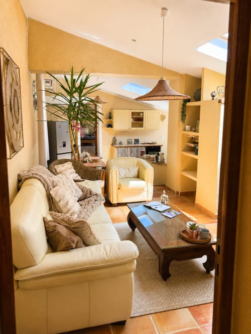 Salon lumineux du Domaine Bellavigne Gîtes à Forcalquier, canapé crème, fauteuil en rotin et plafond aérien