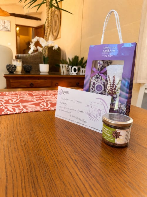 Cadeaux de bienvenue au Domaine Bellavigne Gîtes et Spa : ensemble lavande, mot manuscrit et pot d'épices sur table en bois