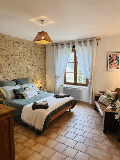 Chambre Gîte Romarin au Domaine Bellavigne avec murs en pierre, vue jardin, lit en bois et carrelage en terre cuite