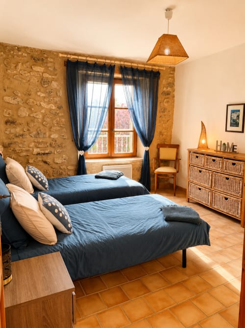 Chambre rustique en pierre au Domaine Bellavigne avec lits jumeaux, carrelage en terre cuite et vue sur le jardin à Forcalquier