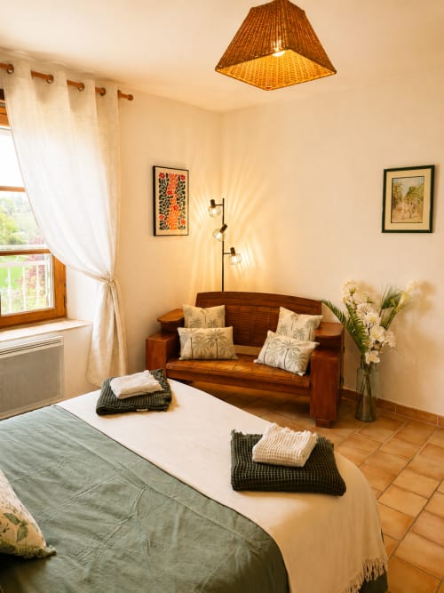 Chambre douillette à Domaine Bellavigne : canapé en bois, lampadaire en rotin et vue sur le jardin à Forcalquier