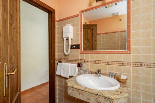 Salle de bains de l'Hotel Balcón De Los Montés avec lavabo blanc, comptoir en granit, miroir encadré et carrelage en terre cuite à Colmenar,