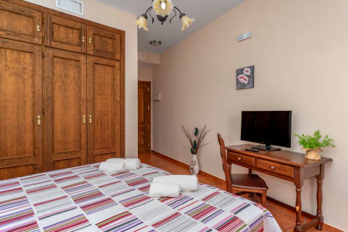 Chambre d'hôtel accessible à Colmenar avec lit à rayures, armoire en bois, bureau avec TV et accès fauteuil roulant