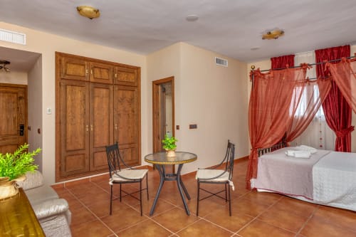 Suite de l'Hôtel Balcón De Los Montés à Colmenar avec coin salon, carrelage en terre cuite, armoires en bois et lit aux rideaux rouges.