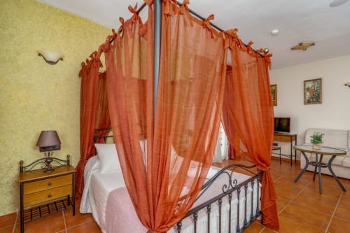 Suite luxueuse avec lit à baldaquin orné et rideaux orange à l'Hôtel Balcón De Los Montés à Colmenar, Espagne