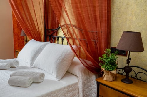 Suite con balcón en Hotel Balcón De Los Montés en Colmenar, con ropa de cama blanca, cortinas rojas y lámpara de escritorio