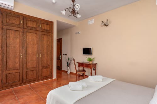 Suite spacieuse à l'Hôtel Balcón De Los Montés avec armoire en bois, lit, TV, bureau et carrelage en terre cuite à Colmenar.